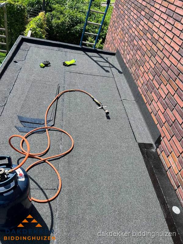 Plat dak met bitumen en brandgereedschap van dakdekkersbedrijf in Biddinghuizen