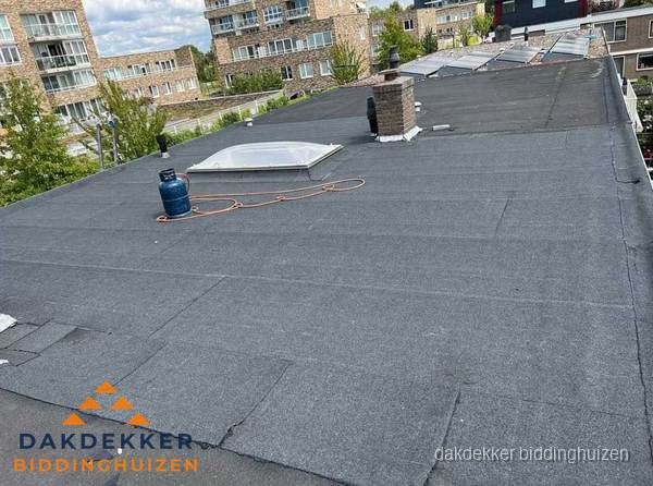 Bitumen dakbedekking op plat dak met lichtkoepel en schoorsteen in Biddinghuizen