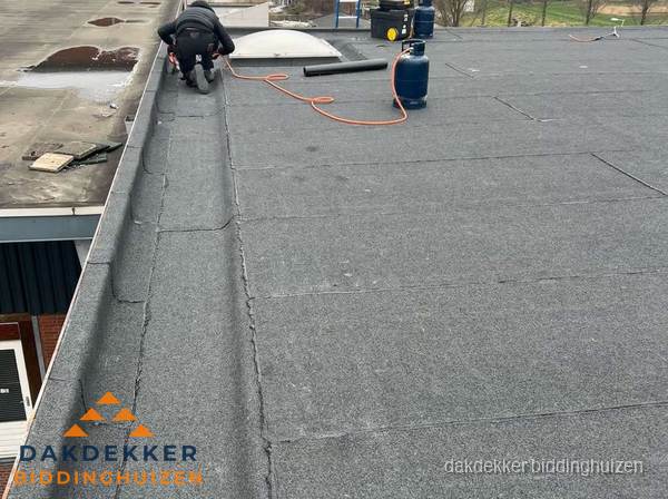 Dakdekker repareert bitumen dakbedekking op groot plat dak in Biddinghuizen